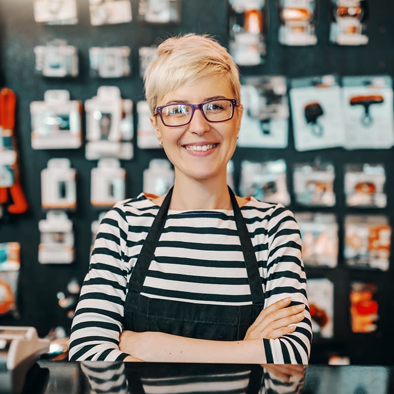 Portrait of a smiling female store employee standing with an apron behind the register in a retail store.