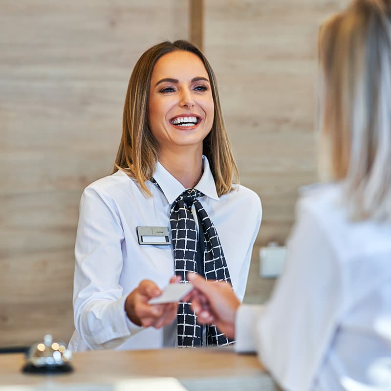 Hotel receptionist smiling while handing over a key card to a guest.