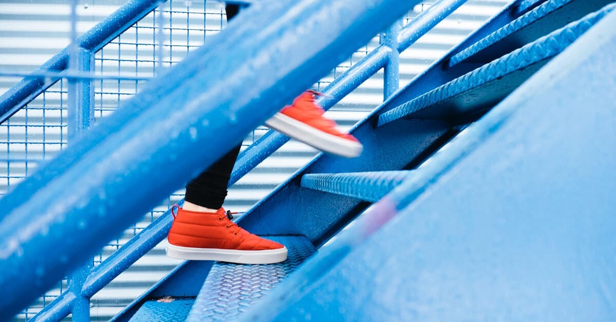 Lower legs of a person in orange sneakers stepping up a blue staircase