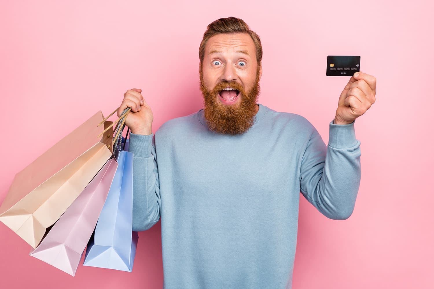 A bearded man screaming against a pink background holding shopping bags and a credit card