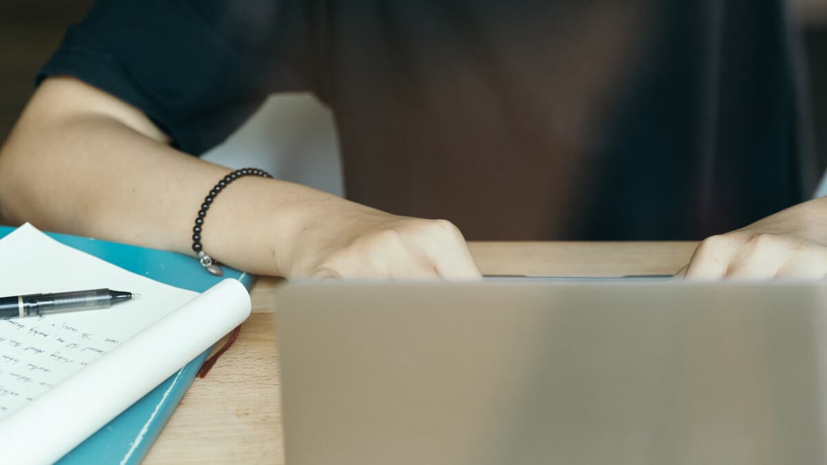 Zoomed in view of a desk with the back of a laptop screen in the foreground and a notepad beside it