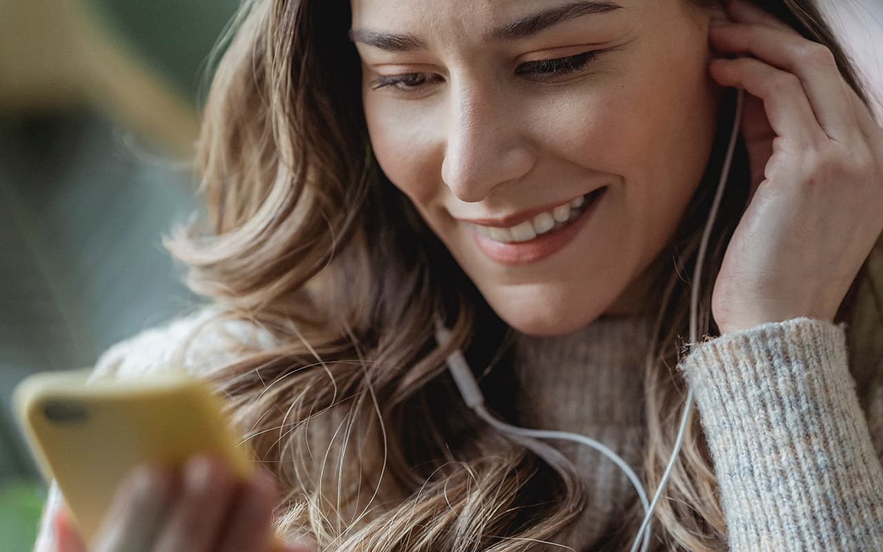 Smiling woman putting in an earphone and looking at her phone doing e-learning