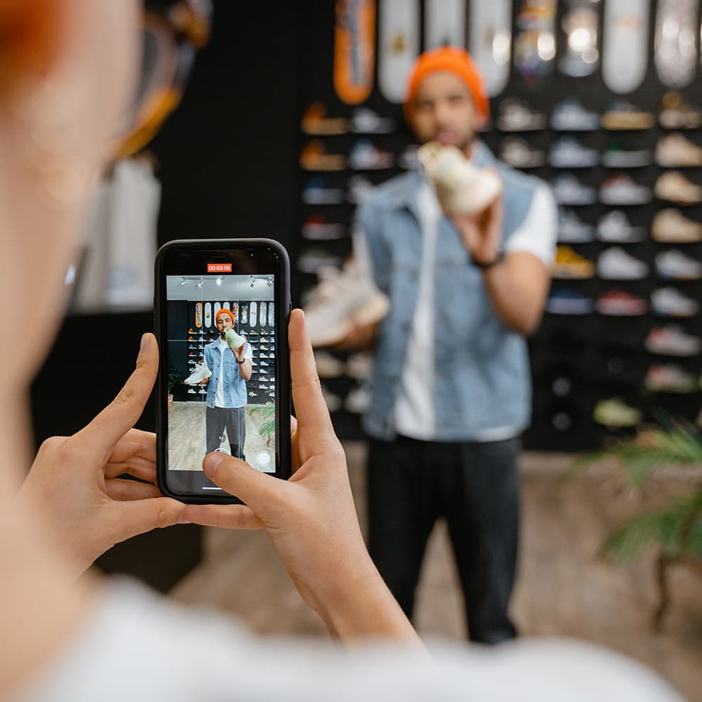 A woman recording video of a male colleague going through product information about shoes in a store.