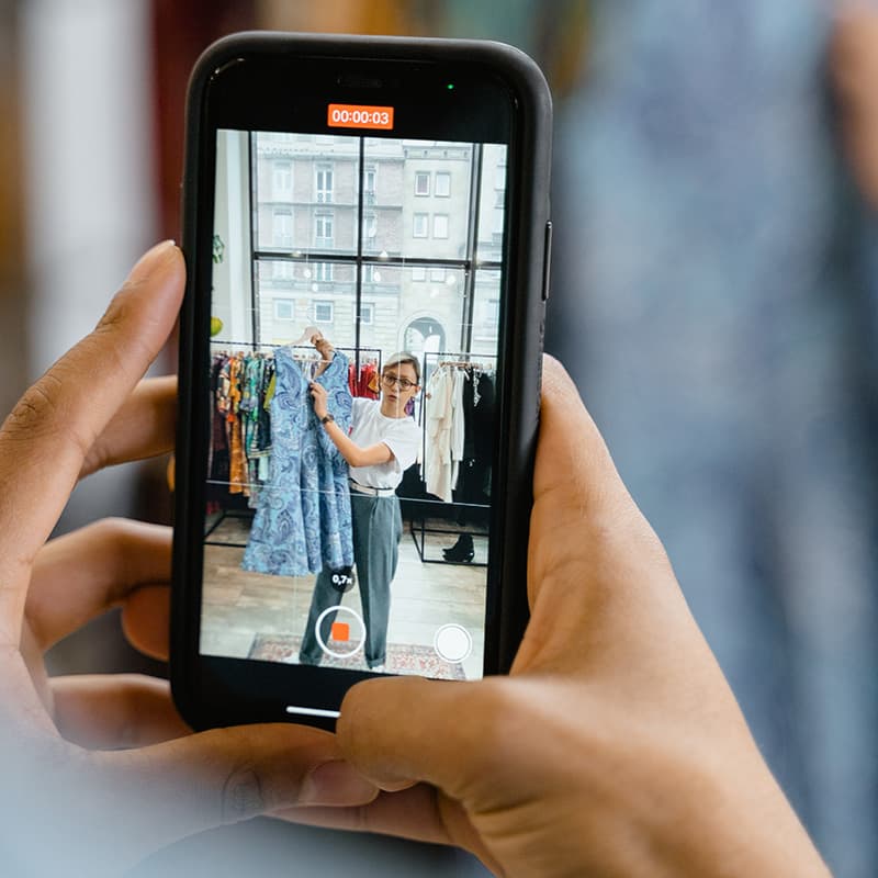 Two hands holding a phone recording video of a female store employee giving a product walkthrough.
