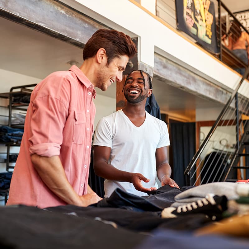 Two male store employees enjoying their work and laughing together while folding clothes
