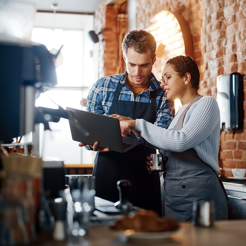Two baristas at a cafe looking at internal information on a laptop, one pointing something out to the other