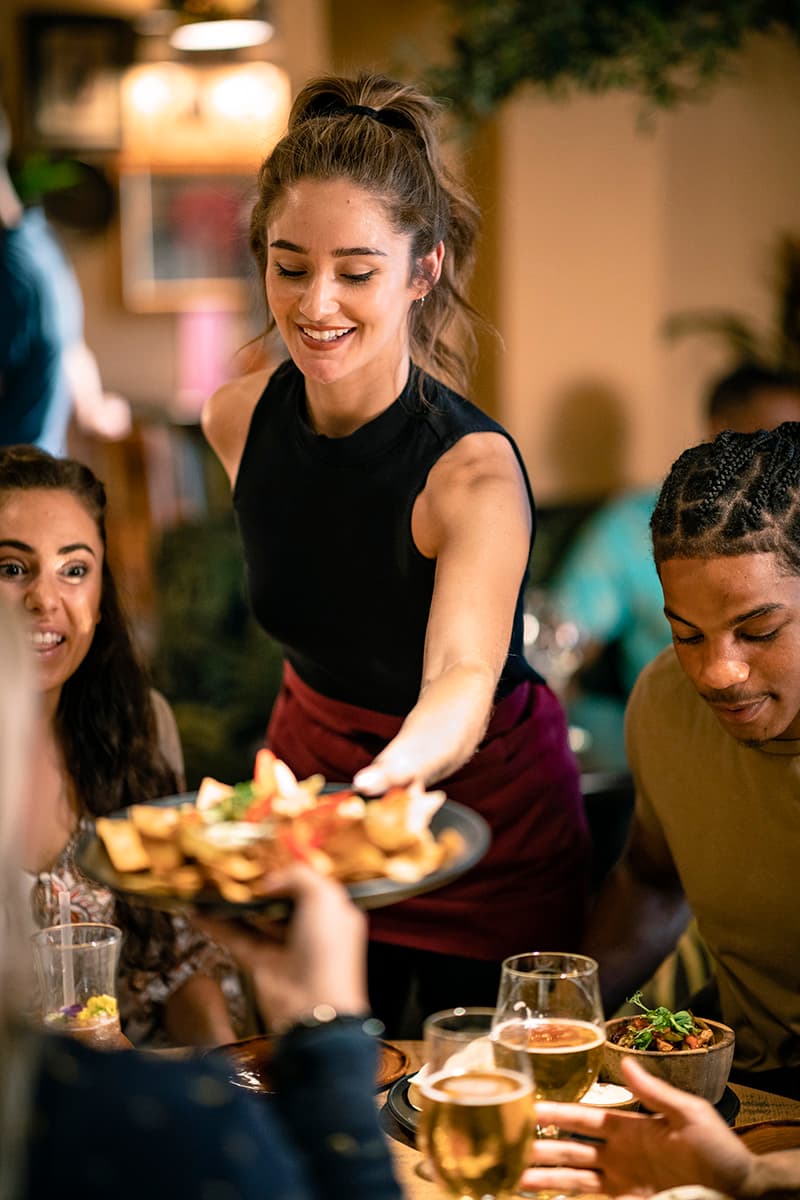A happy and service-minded waitress handing over a plate to a guest in a restaurant.